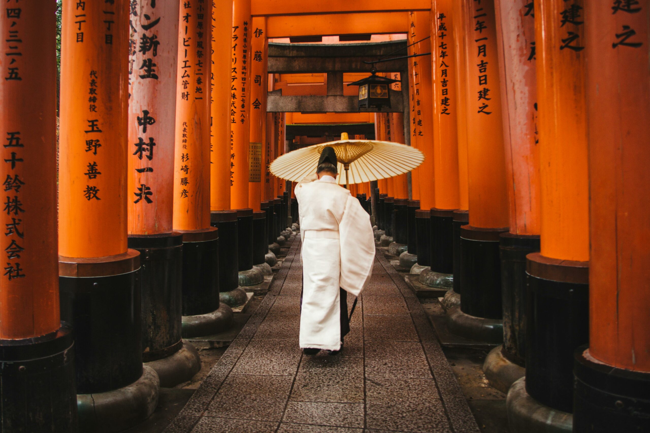 A person in traditional attire walks through the iconic torii gates at Fushimi Inari Shrine, Kyoto.